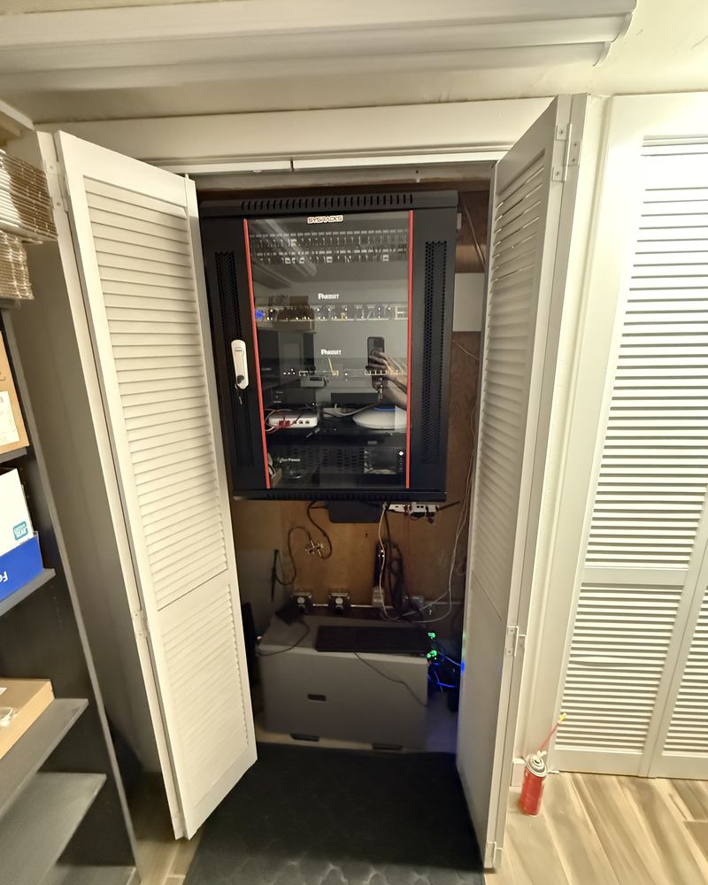 The same closet after remediation: an enclosed wall-mount rack holding patch panels, switching and a UPS, with the floor clear