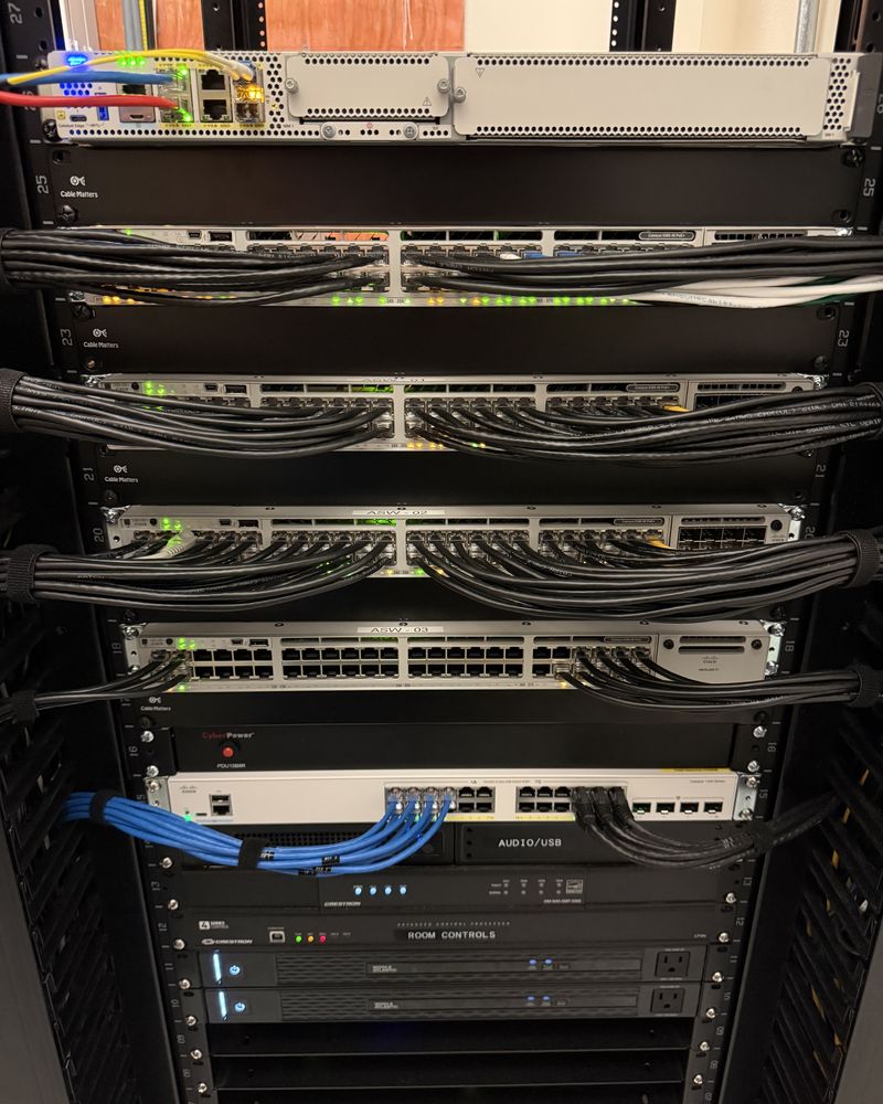 A stack of network switches with patch cords routed through horizontal cable management between each panel